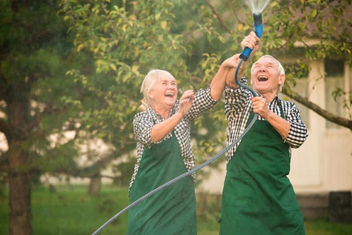 An older couple using a Qwickhose starter set spray nozzle in their garden while laughing together