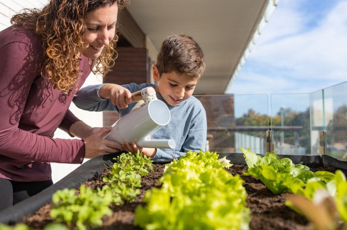 A parent and child watering plants together in an urban garden